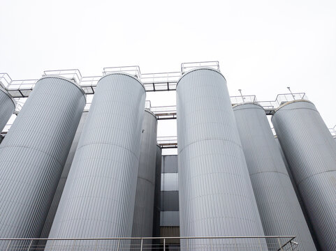 Low angle view of large industrial stainless steel silos and storage tanks at a food processing plant or brewery, modern manufacturing facility architecture