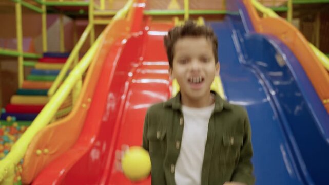 Joyful cute little African American boy in the game center while holding colored balls, jumping, slide on the background. Slow motion