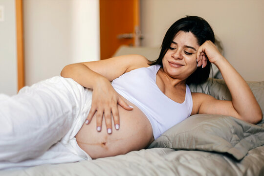 Pregnant woman lying comfortably on a bed and touching her baby bump, enjoying a calm and peaceful moment of connection during pregnancy.