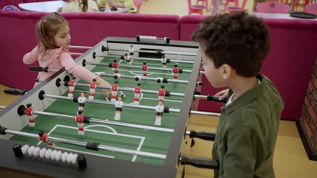Joyful little boy and girl playing football table toy in game center. Happy childhood. Kid playing table games. Slow motion