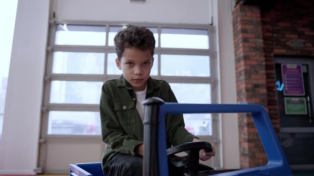 African American little boy driving big toy car and having fun playing in game center. Slow motion