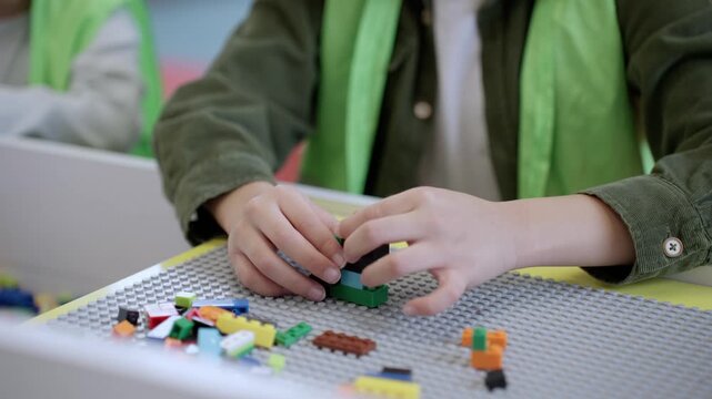 Hands of little boy in safe waistcoat playing with toy colorful blocks on the table in game center. Selective focus. Slow motion