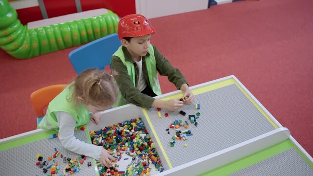 Two kids wearing waistcoats playing with colorful blocks in educational games center. Top view. Slow motion