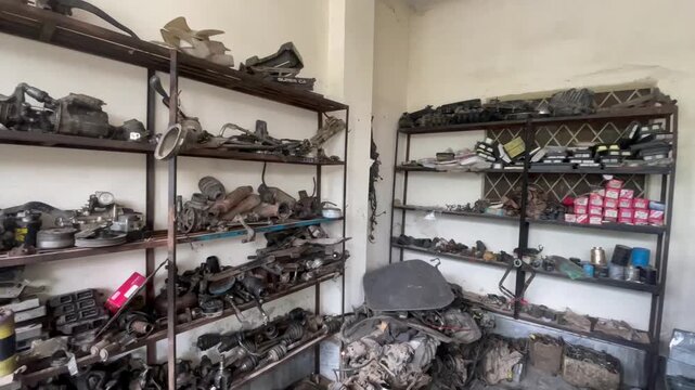 Wide Angle View of Auto Mechanic Workshop with Used Car Parts on Shelves, vehicle repair shop, including engines, tools, and mechanical components placed in an organized yet rugged setting. 