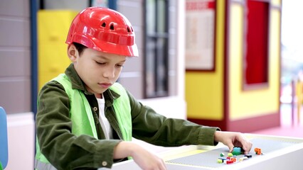 Cute African American boy in helmet and waistcoat playing with colorful toy blocks, building tower in game room. Slow motion. Childhood, entertainment, profession concept © Vlad