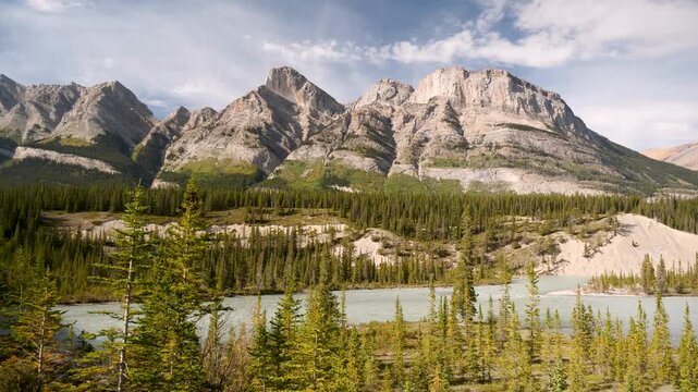 Turquoise alpine lake below towering peaks, evergreen forest foreground, jagged limestone mountains, soft cloud shadows, glacial sediment shorelines, tranquil reflections, Canada
