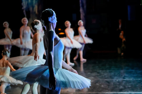 ballerina performing on stage in a ballet production in white costume.