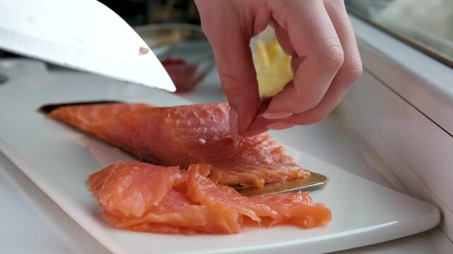 Woman hands carefully take bones out of sliced lightly salted red fish. Home kitchen preparation, salmon fillet ready for serving or cooking.