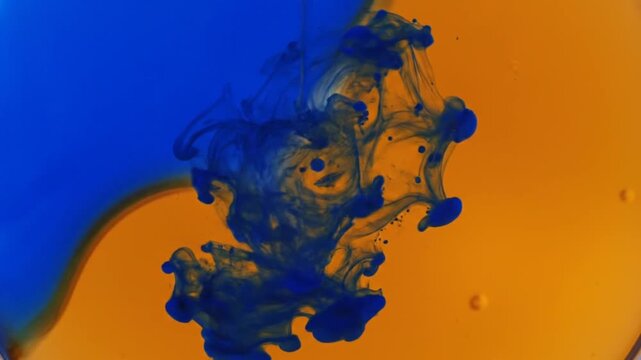 Blue ink dissolving in orange liquid, abstract fluid dynamics and color mixing