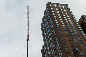 Fototapeta premium Construction site shows tall crane beside modern building in urban setting during cloudy day