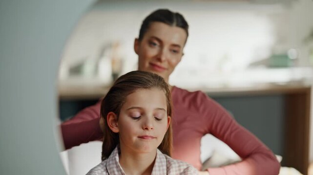 Mother combing daughter hair in mirror doing haircare routine at home closeup