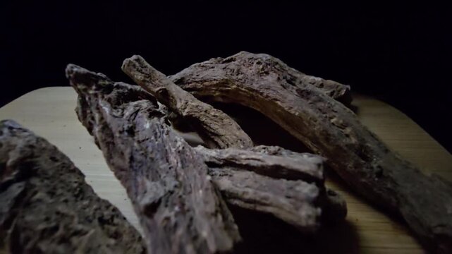 Macro shot of raw Indian Costus roots (Saussurea costus) on a wooden surface. High-quality footage showcasing the natural, dried woody texture of this ancient medicinal herb.