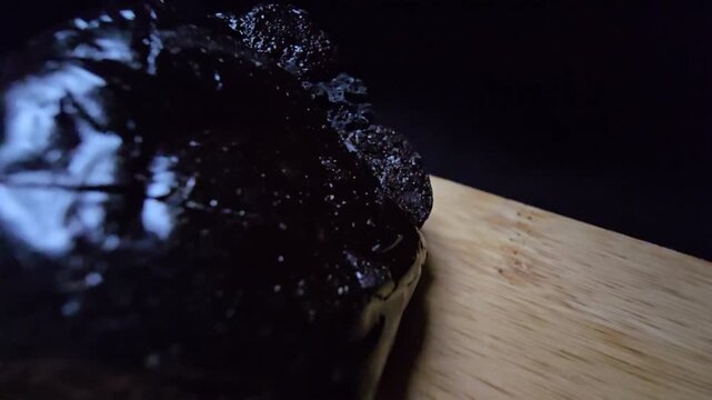 Macro shot of raw Shilajit (Asphaltum punjabianum) on a wooden surface. High-quality footage showcasing the dark, glossy, and resinous texture of this ancient Himalayan mineral pitch.