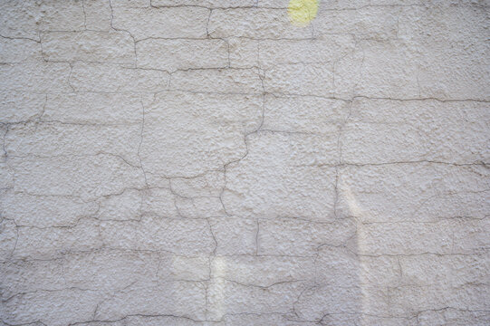 Close-up view of a weathered, textured concrete wall with fine cracks and a subtle yellow mark