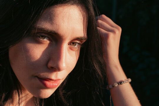 Close up portrait of young woman with hand in hair in warm sunlight