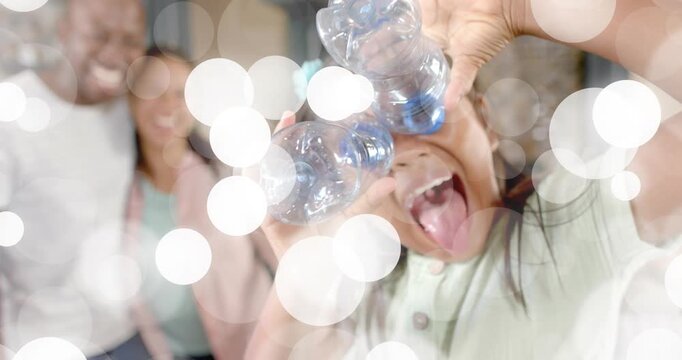 Child lifting clear bottles to eyes at home, bokeh overlay accenting playful gag to amuse parents