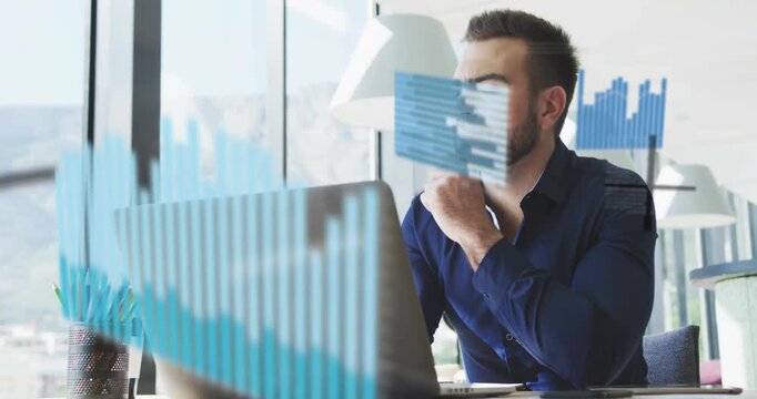 Man in his 30s wearing navy shirt sitting in office using laptop watching animated data charts