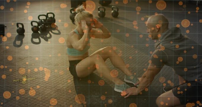 Doing crunches after coach holding feet, trainee in sportswear curling for core, kettlebells in gym