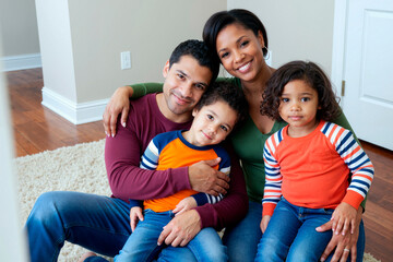 Portrait of multiethnic young family sitting closely, smiling at camera in new home, expressing bonding and relocation concept. Ideal for housing, insurance, parenting, mortgage marketing