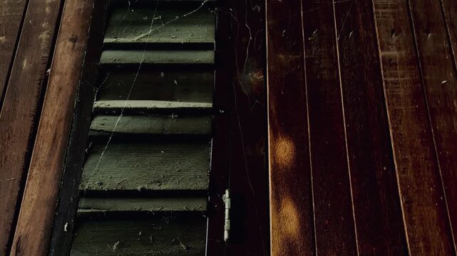 A close-up image of the wall of an old wooden house, more than a century old, reveals the texture, cracks, and dust and cobwebs that have been left untouched by time, reflecting the historical archi