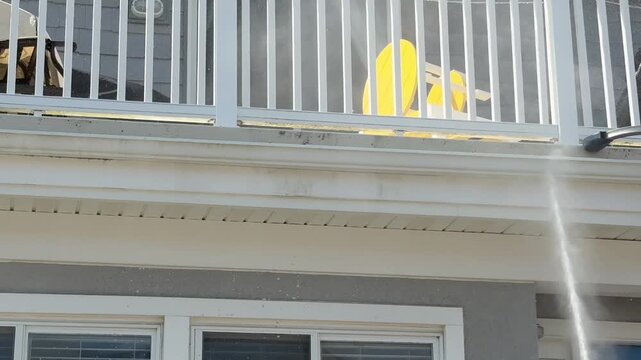 Power washing dirt off of the side of a porch of a house with a stream of water
