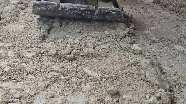 Slow motion front shot of a vibrating plate machine compacting dry soil.