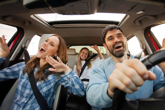 Three family members having joyful car ride, singing and dancing together during sunny afternoon drive, parents and daughter enjoying trip