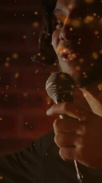 Vertical video: Warm glow showing male singer in dark shirt holding wired mic, singing in studio
