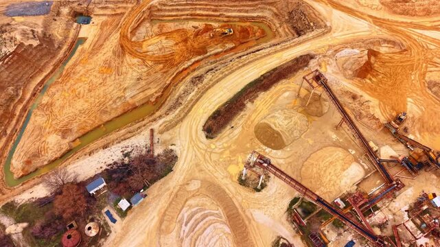 High angle view of industrial sand quarry and conveyor structures. Wide aerial shot of open pit mine featuring sand piles, processing equipment and heavy machinery.