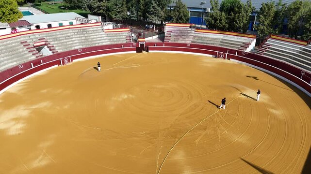 Workers preparing bullring arena with sand and water in traditional Spanish plaza de toros