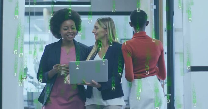 Walking two women in blazers consulting laptop in glass corridor, green overlay intensifying
