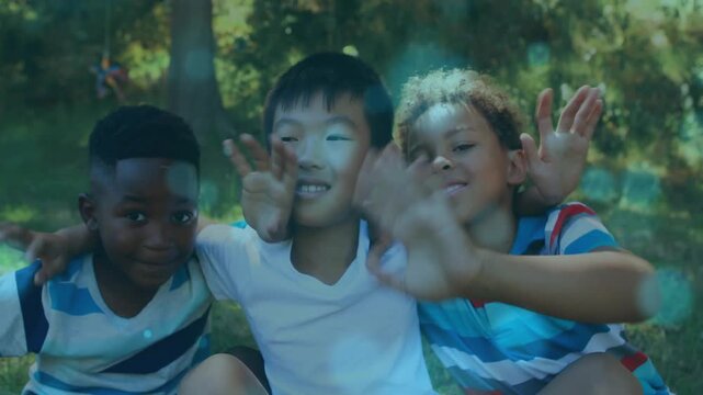Vertical video: Reaching three boys hugging in park, striped tees touching cam amid pinwheel bokeh