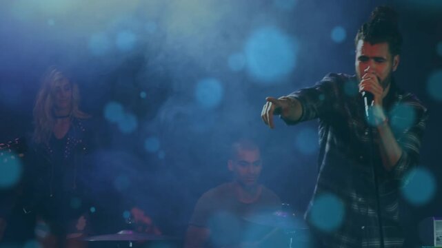 Lead singer moving into frame, gripping mic and singing, engaging fans, blue bokeh on music stage
