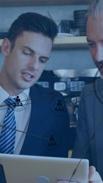 Vertical video: Left man tapping tablet, pair leaning in mapping business network, nodes expanding
