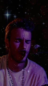 Vertical video: Purple light cueing singer tapping stick, singing to mic on stage with beads, stars