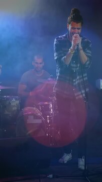 Vertical video: Singer starting verse, gripping mic, drummer keeping beat, expressing music emotion