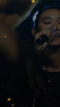 Vertical video: Female singer with mic singing music for fans, arm blocking view, gold dust overlay