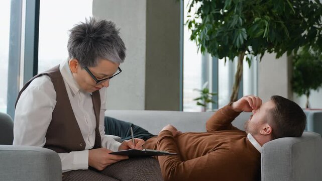 Stressed man lying on couch during therapy session with psychologist