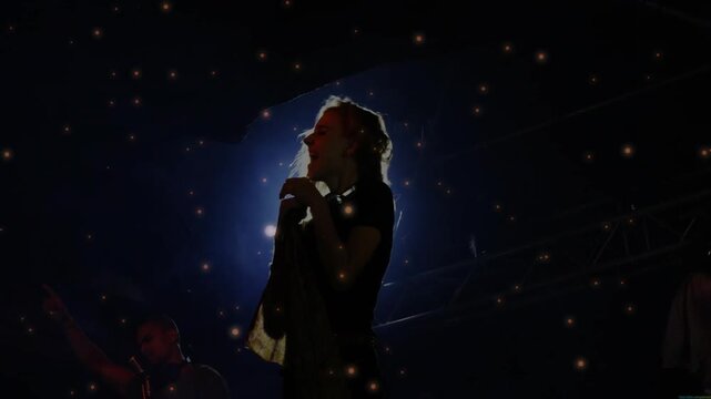 Rear spotlight flaring as lead singer flipping hair, singing into mic for concert, sparks drifting