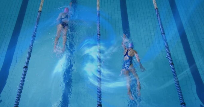 Two swimmers starting mid-stroke and training steady freestyle in lap pool, creating blue trails