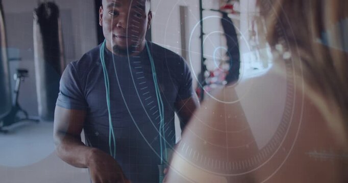 Starting trainer in dark tee correcting client form in gym, gesturing with jump rope and HUD