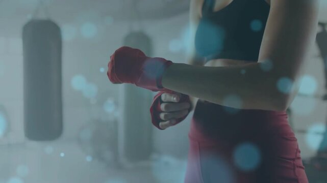 Boxer grabbing red wraps, winding knuckles and tightening for training amid heavy bags, blue bokeh