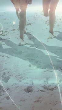 Vertical video: Sunlight starting close-up, family legs walking, leaving footprints toward surf