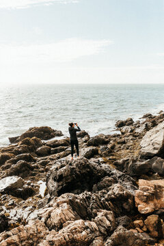 Young woman photographing Bass Harbor Light Station from rocky c