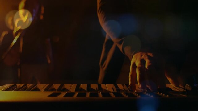 Keyboardist starting on music cue, playing synth backing horn while warm bokeh crossing keys