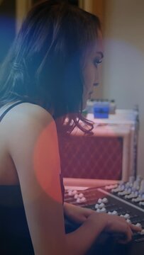 Vertical video: Woman audio tech responding to blue light, adjusting faders to balance studio mix