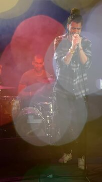 Vertical video: Cue firing, vocalist singing into mic, drummer keeping beat to raise song mood