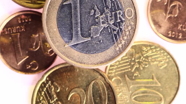 Top-down close-up of a single euro coin standing out among scattered euro cents and Turkish kurus coins with shallow depth of field on white background