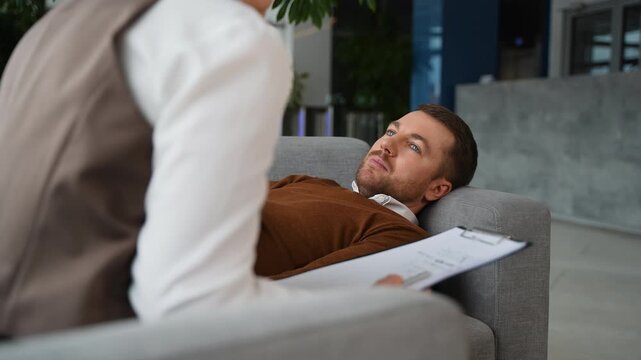 Male patient lying on couch talking to psychologist during therapy session
