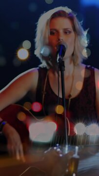 Vertical video: Focus shift revealing singer strumming guitar and singing for music crowd